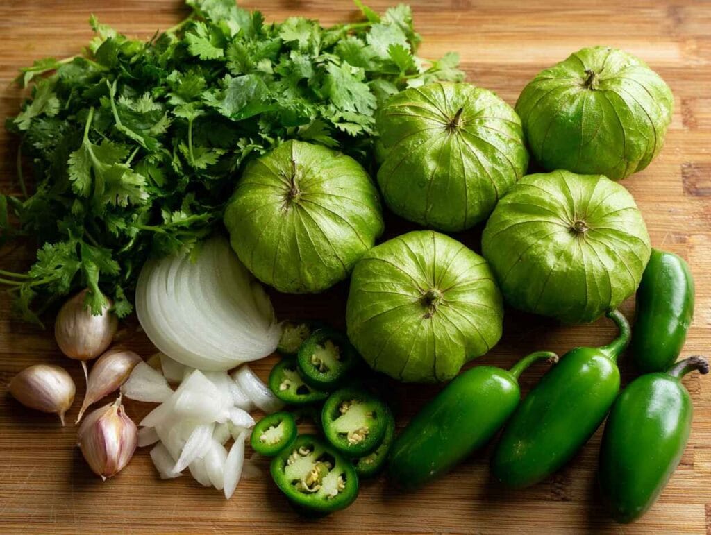 Fresh green chilies, tomatillos, garlic, onion on cutting board