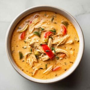 Creamy Cajun chicken soup with tender shredded chicken, colorful vegetables, and bold Cajun spices in a modern, minimal bowl with a rich golden broth.