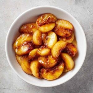 Caramelized fried apples in a white bowl coated with butter, sugar, and cinnamon for a warm fall dessert