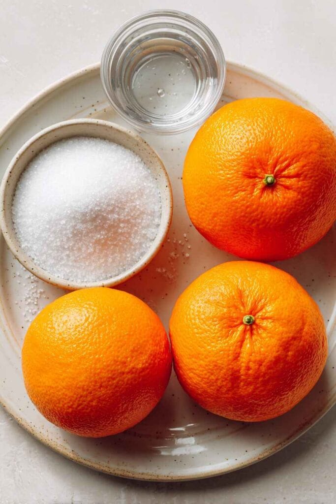 Oranges, sugar, and water arranged on a plate