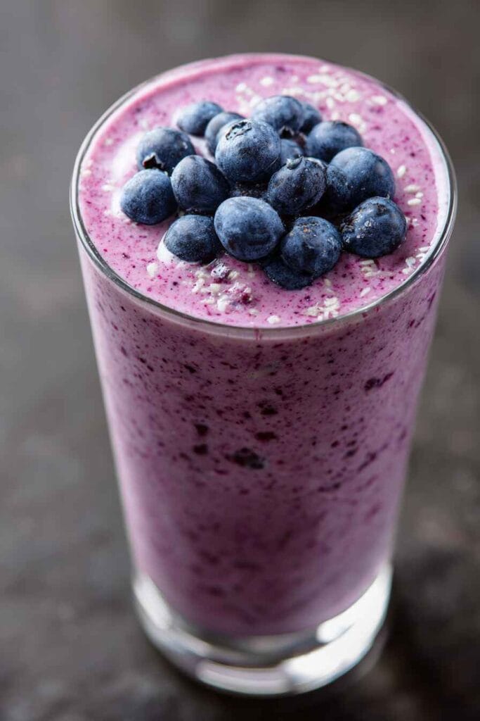 Blueberry yogurt smoothie in a tall glass topped with whole blueberries