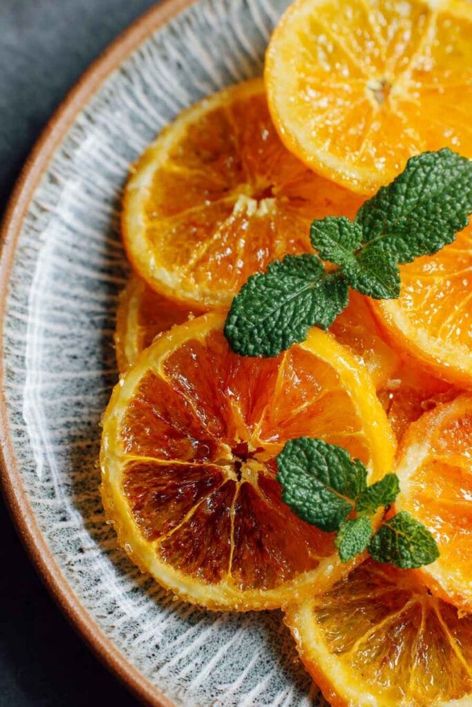 Candied orange slices with glossy sugar coating, arranged on a ceramic plate and garnished with fresh mint