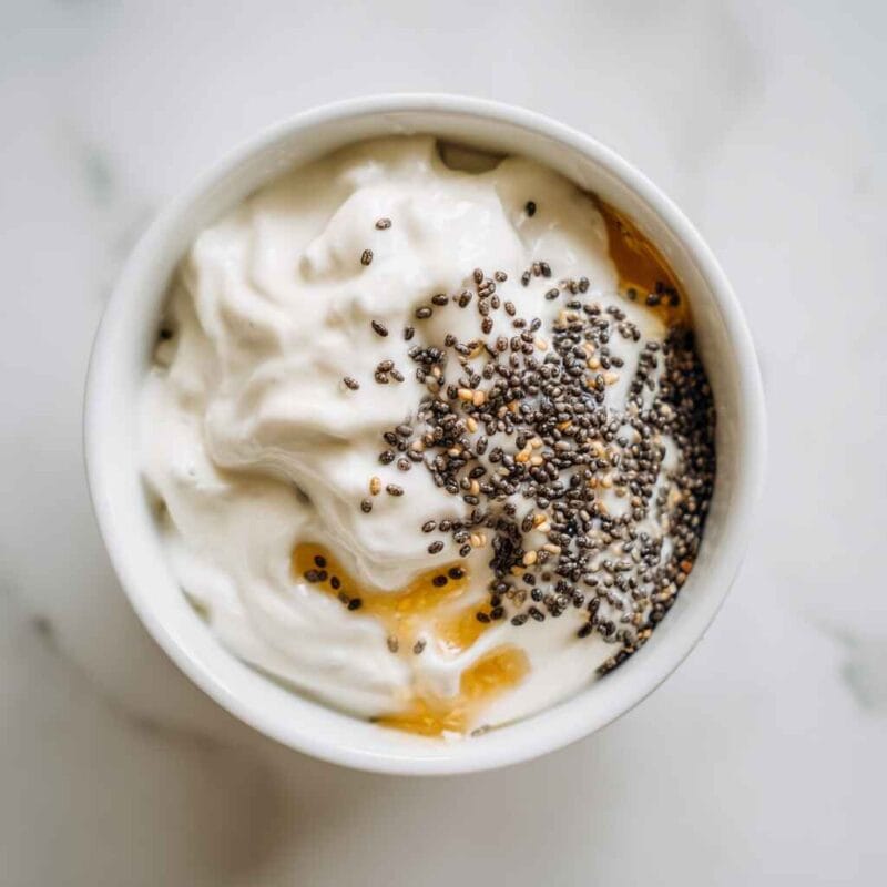 chia seeds honey and milk added to greek yogurt in a mixing bowl before stirring