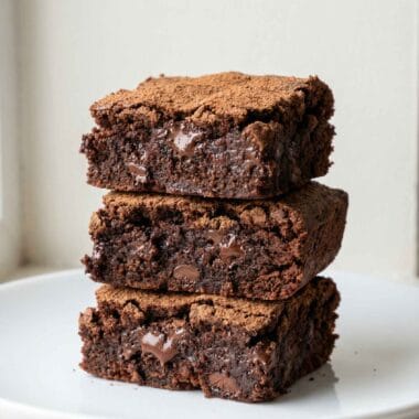 Chocolate brownies with protein powder stacked on a white plate with cocoa dusting and fudgy melted center
