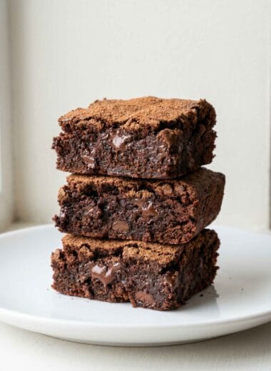 Chocolate brownies with protein powder stacked on a white plate with cocoa dusting and fudgy melted center