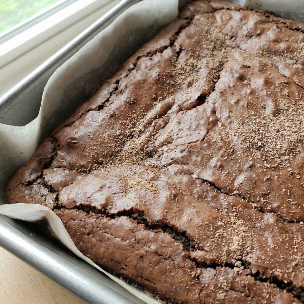 Freshly baked chocolate brownies with protein powder cooling in a parchment-lined pan