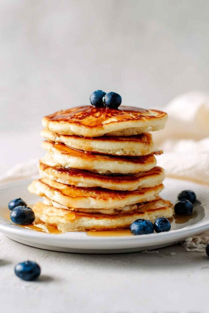 High protein cottage cheese pancakes stacked with blueberries and light maple syrup on a white plate.