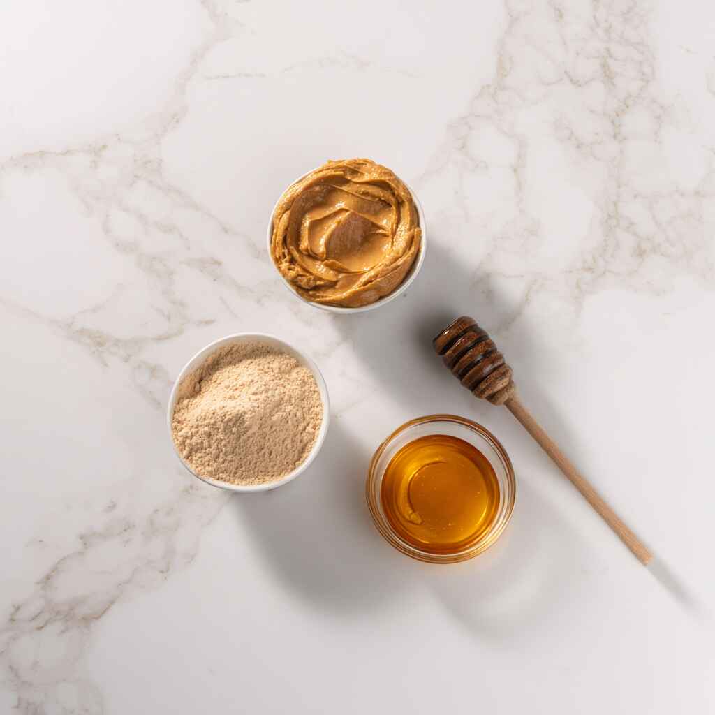 Peanut butter, protein powder, and honey arranged on a white marble surface