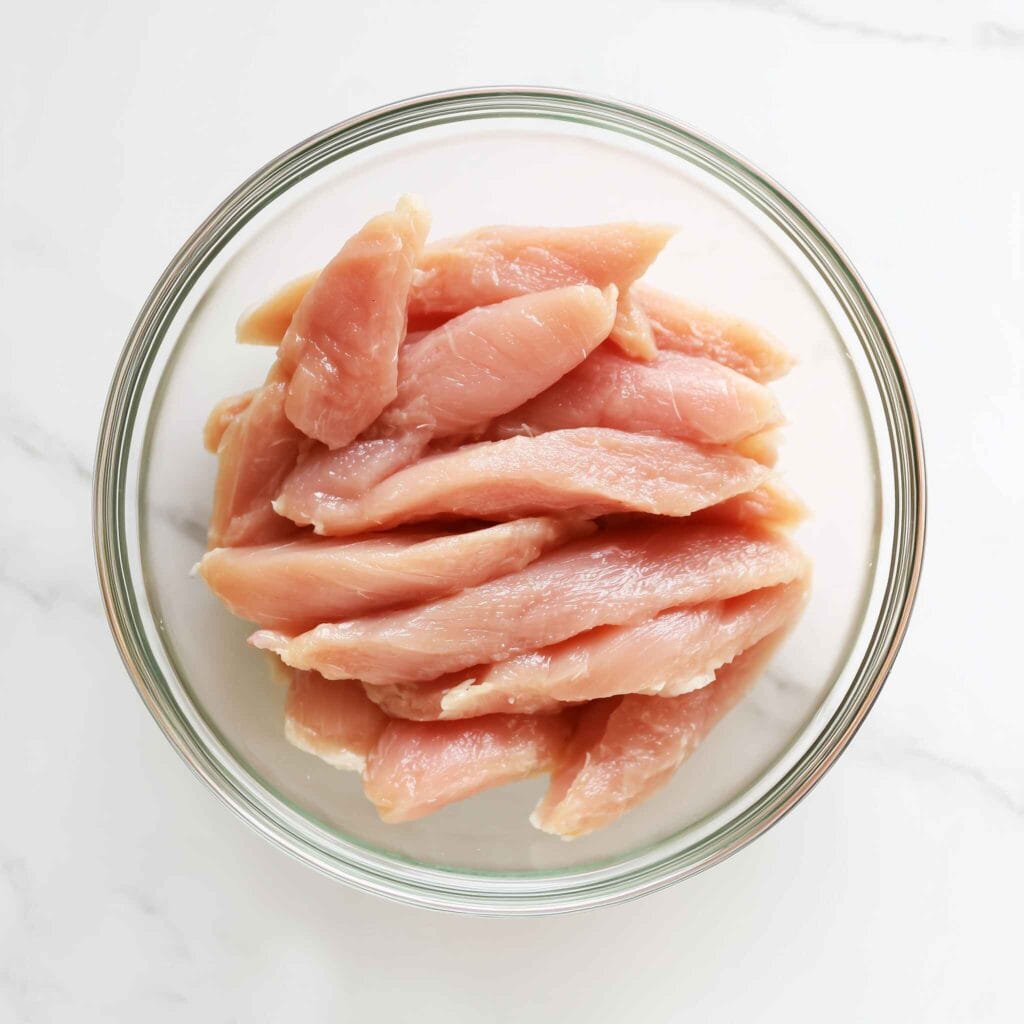 Raw chicken breast strips prepared in a bowl for low calorie chicken strips