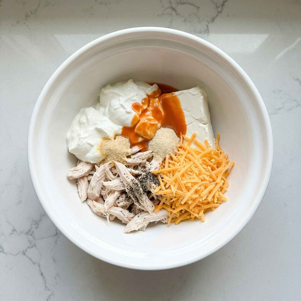 Shredded chicken and ingredients placed in a bowl before mixing.